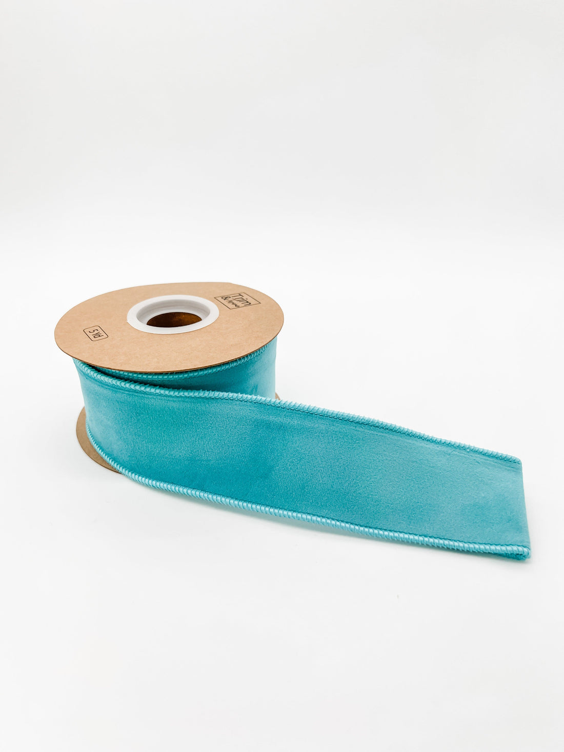 Turquoise velvet ribbon on a cardboard reel against a white background