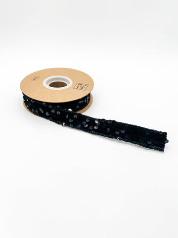 Roll of black ribbon with sequins on a white background