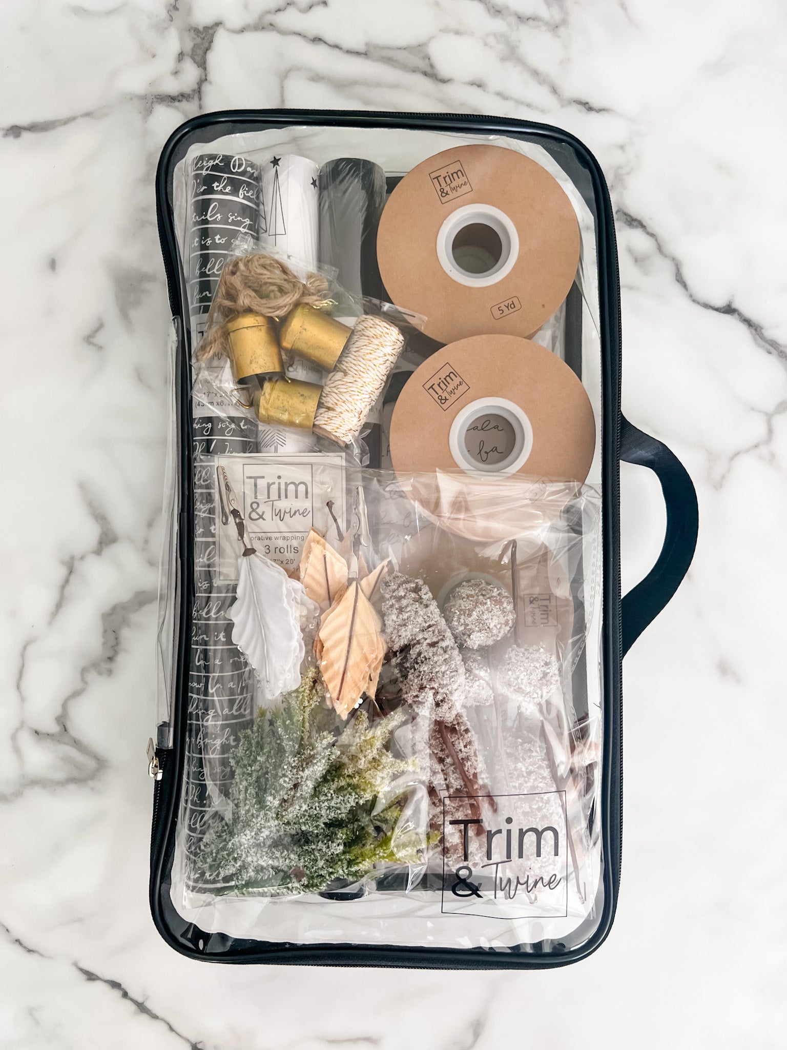 A clear zippered storage bag with a black handle and items inside, laid flat on a white marble surface. 