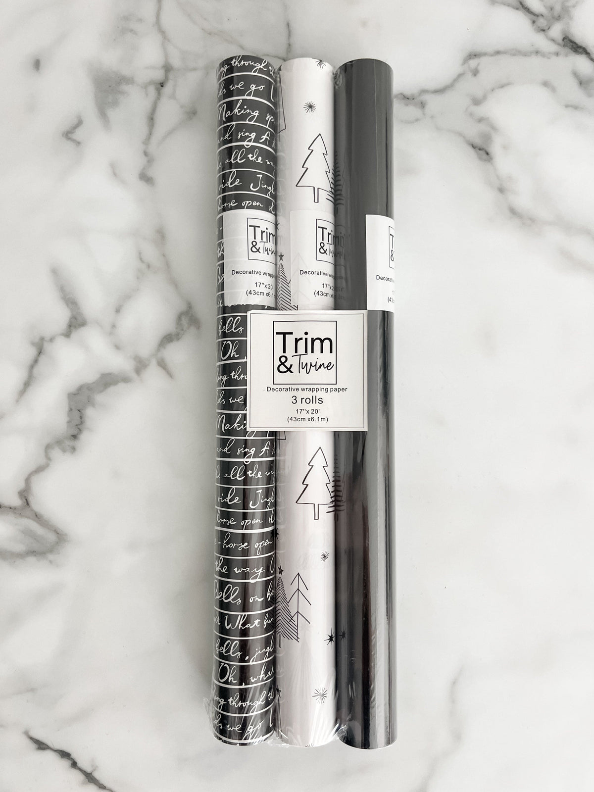 three rolls of wrapping paper. One black and white design with jingle bell words, one black and white tree design and one solid black design