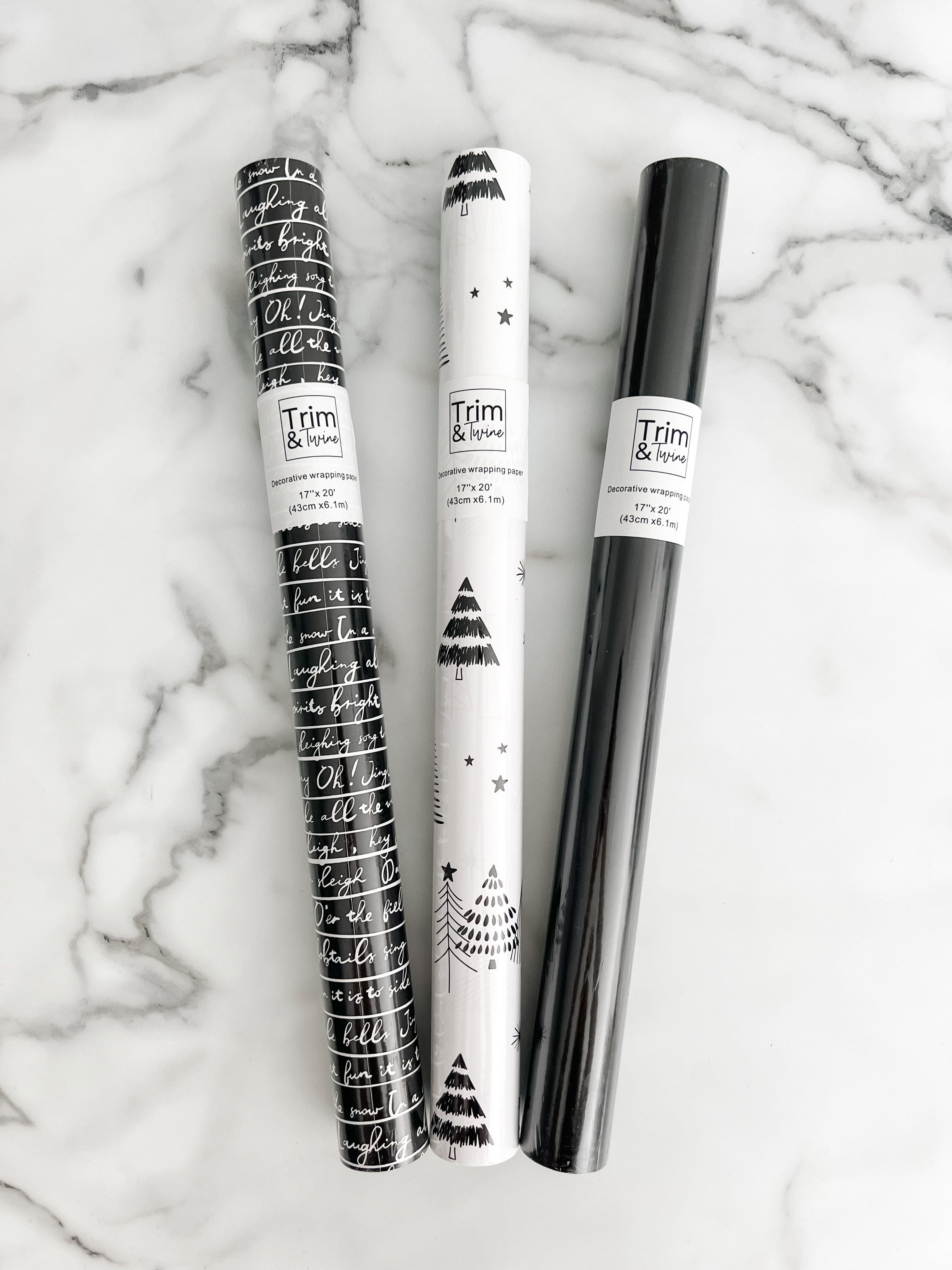 three rolls of wrapping paper. One black and white design with jingle bell words, one black and white tree design and one solid black design