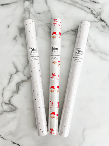 Three rolls of wrapping paper with Santa Claus design, metallic gold stars, and metallic silver dots, placed on a marble surface.