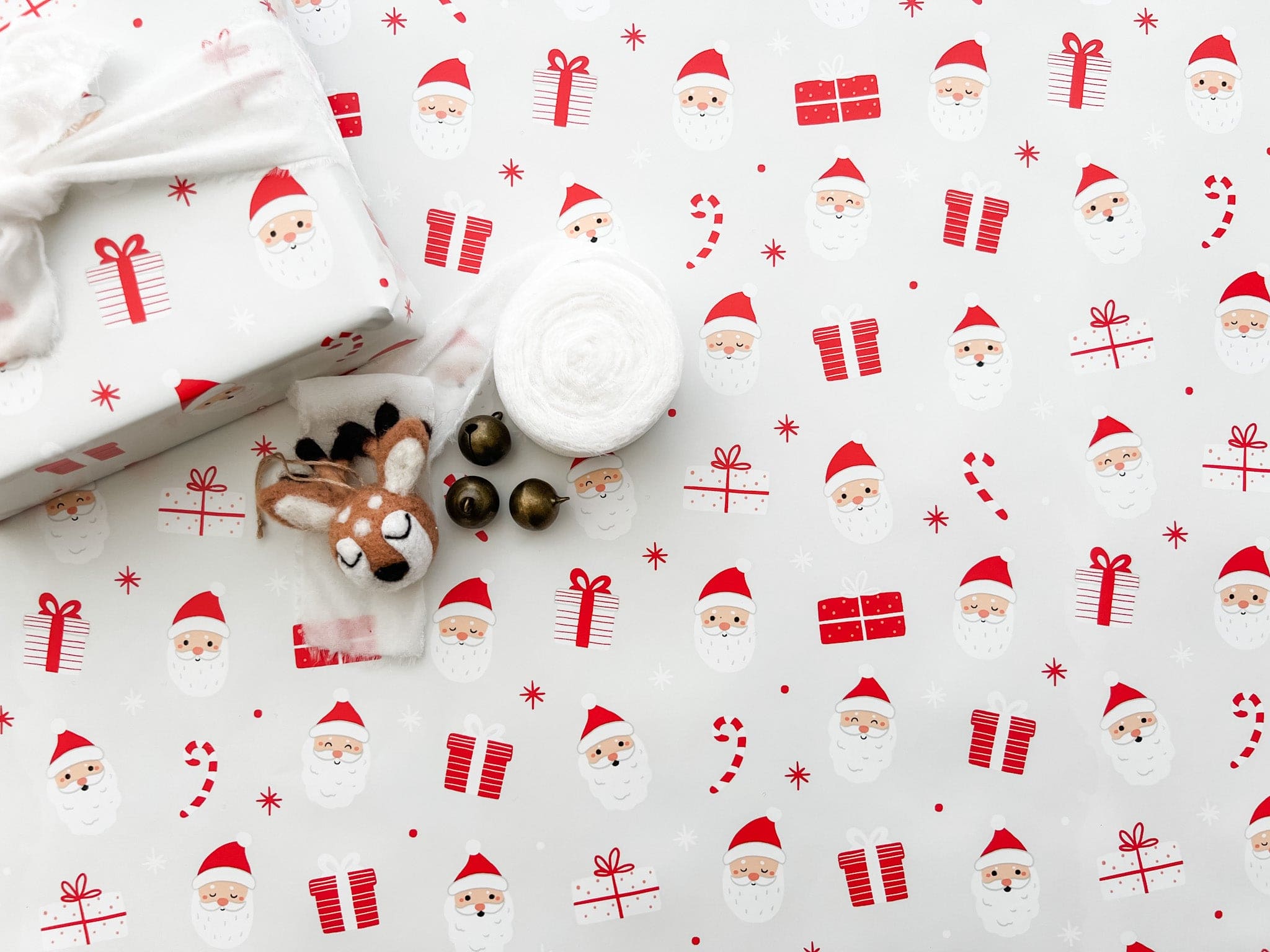 A rolled out piece of wrapping paper with a Christmas theme, featuring illustrations of Santa Claus and holiday motifs in red and white colors.