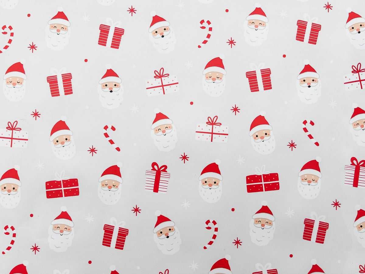 A rolled out piece of wrapping paper with a Christmas theme, featuring illustrations of Santa Claus and holiday motifs in red and white colors.