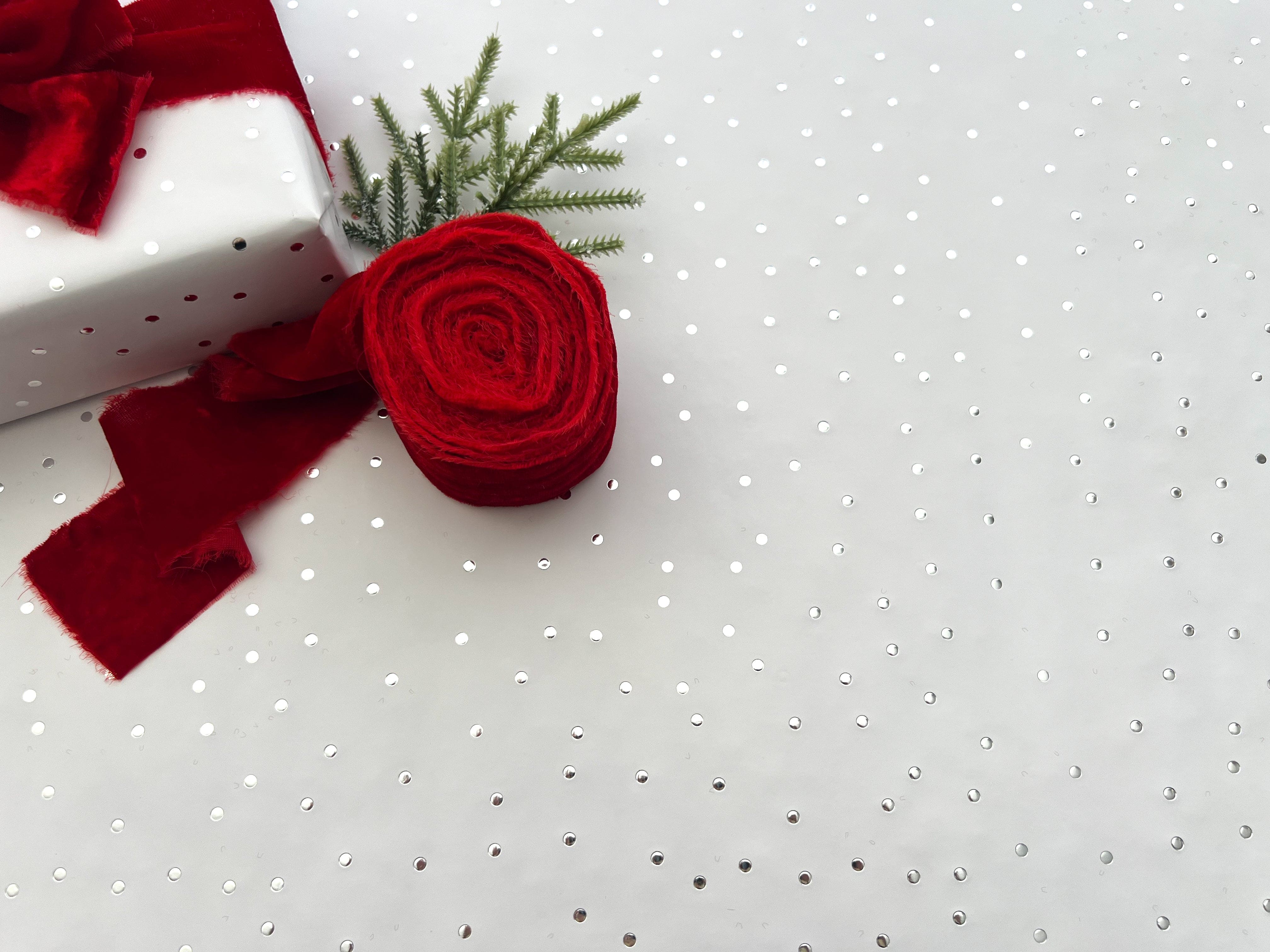 A single roll of silver metallic polka dot wrapping paper with a red ribbon, presented against a white background.