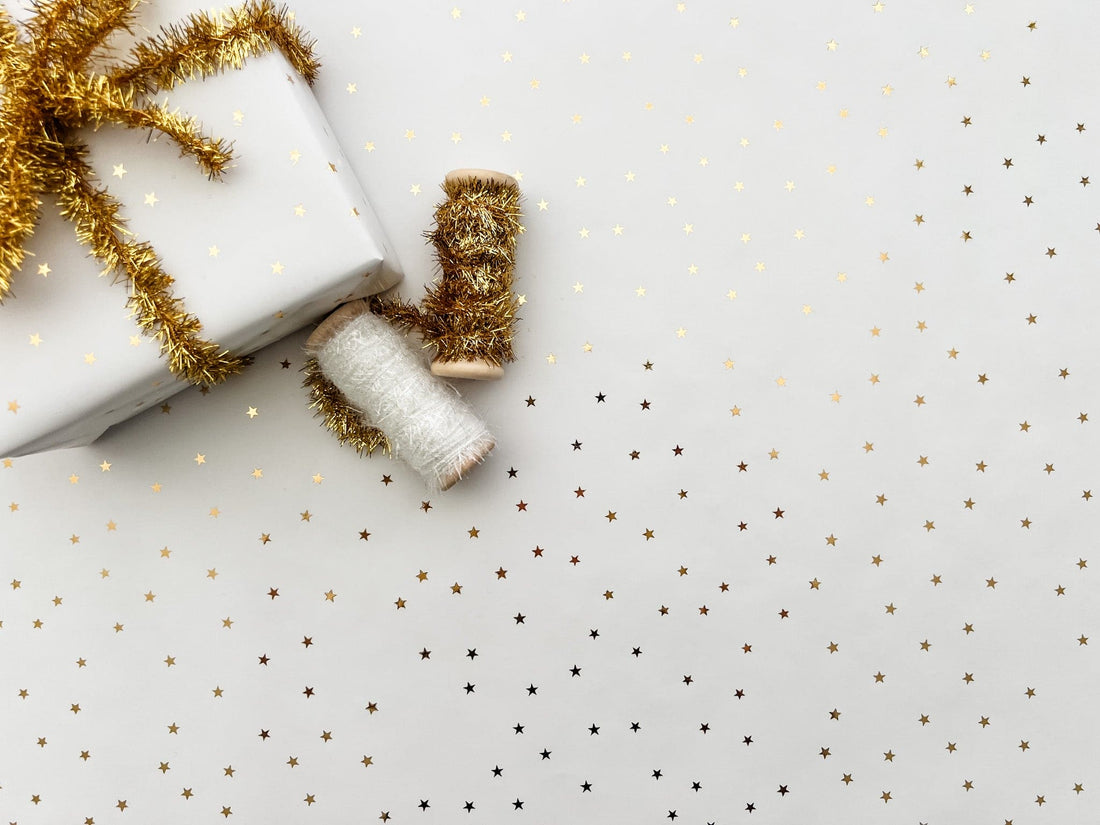 Wrapping paper with gold metallic stars on a white background shown with tinsel.