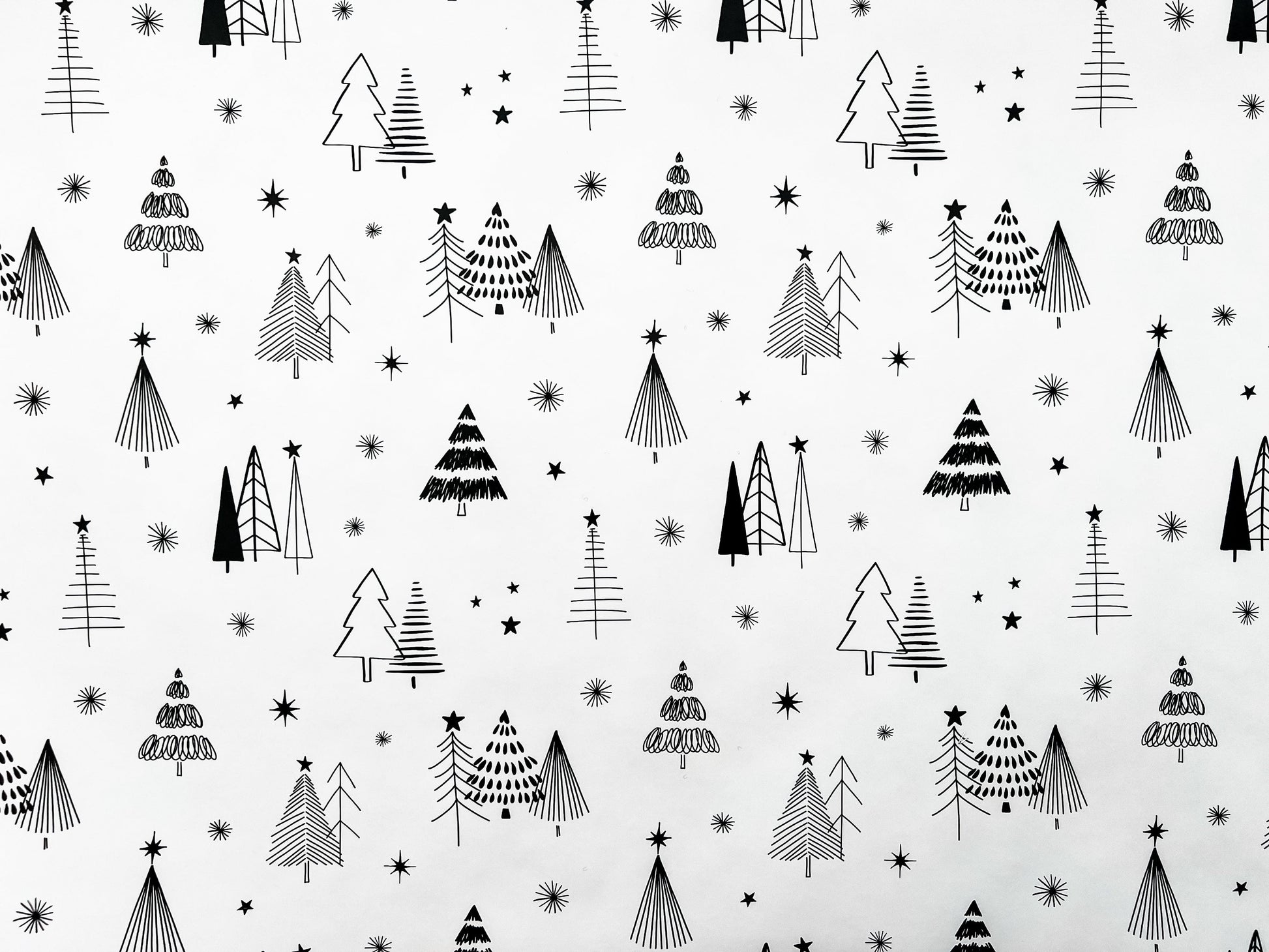 A rolled out piece of wrapping paper with a Christmas theme, featuring illustrations of black and white trees and stars.
