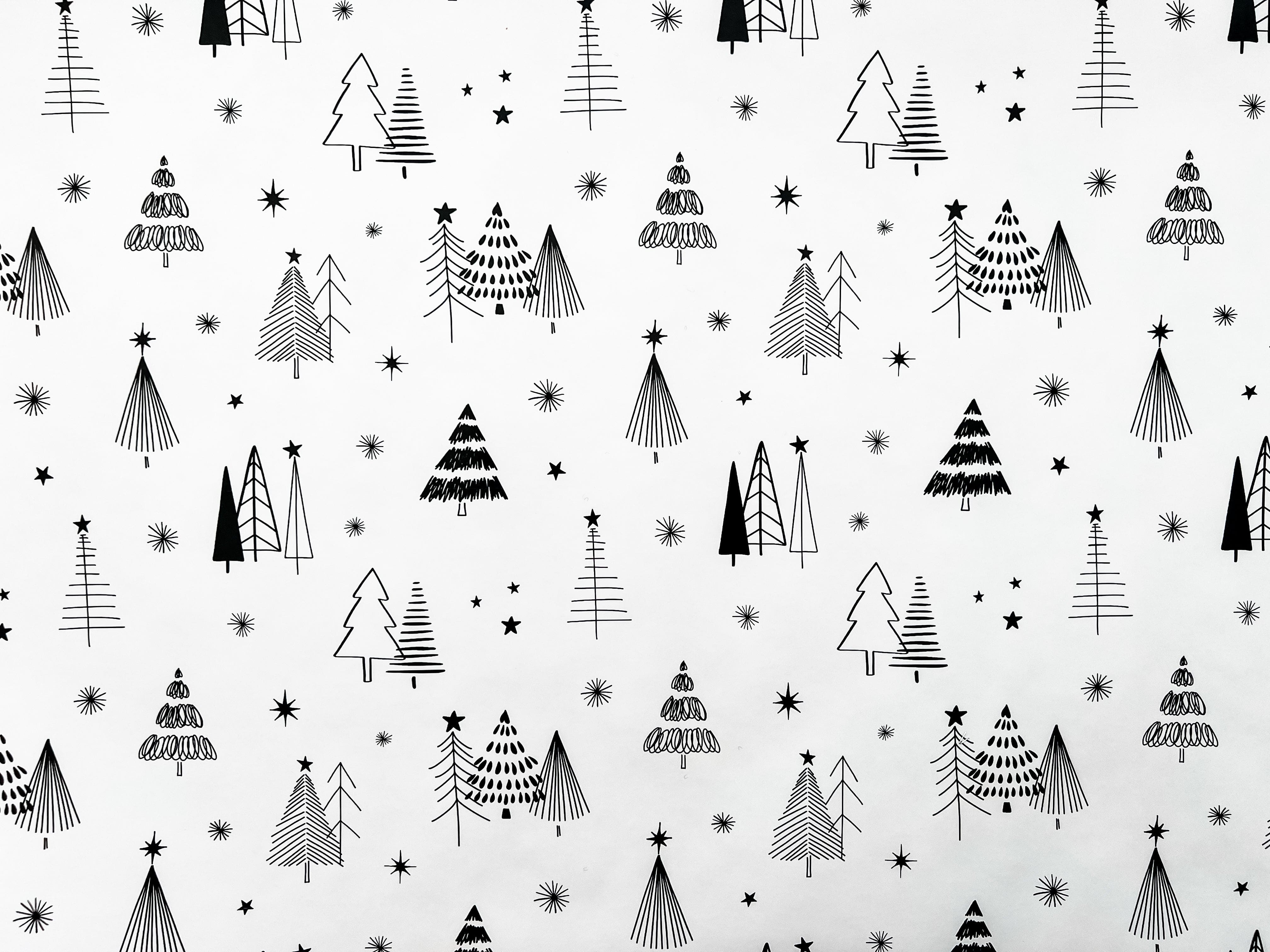 A rolled out piece of wrapping paper with a Christmas theme, featuring illustrations of black and white trees and stars.