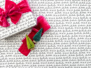 A roll of Christmas wrapping paper with the phrase 'Fa La La' repeated in a modern, monochrome black and white design. The paper is displayed with a close-up of the text pattern.