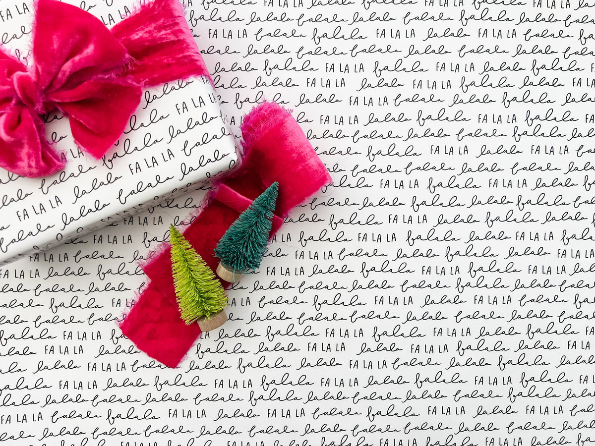 A roll of Christmas wrapping paper with the phrase 'Fa La La' repeated in a modern, monochrome black and white design. The paper is displayed with a close-up of the text pattern.