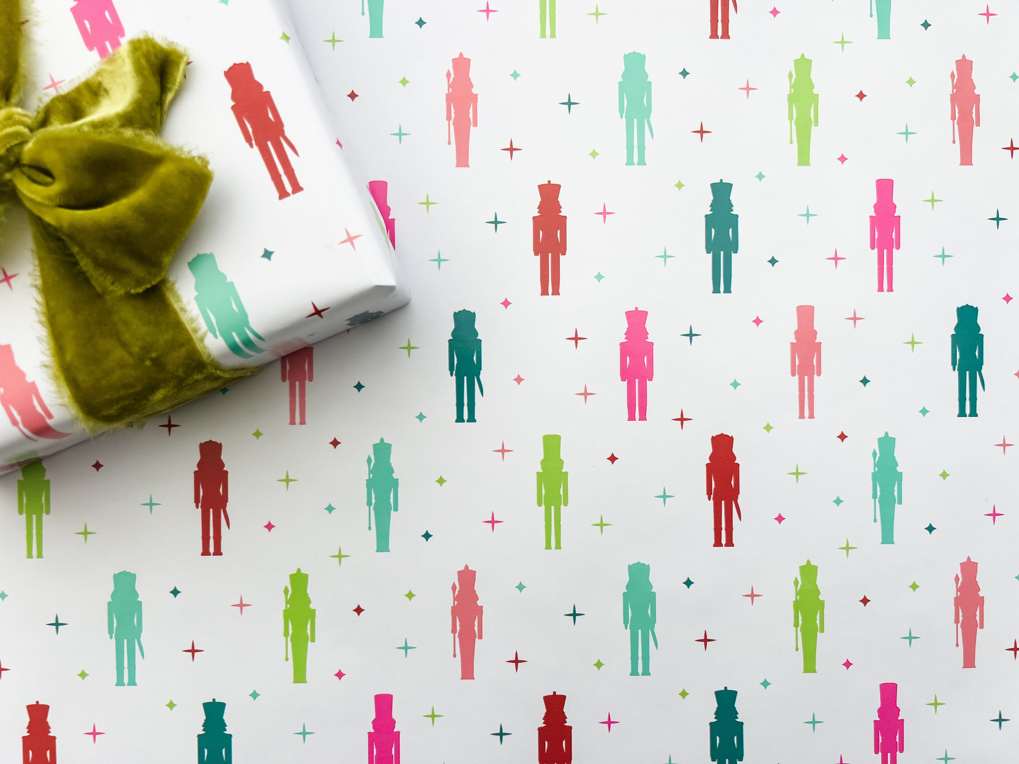 A laid out roll of wrapping paper with a colorful nutcracker pattern featuring nutcracker figures, displayed alongside a green ribbon.