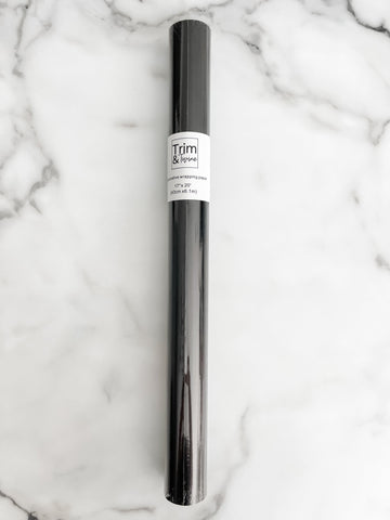 A roll of solid black wrapping paper with a label in the middle, placed on a marble surface.