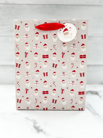 A festive Santa Claus design gift bag with a red ribbon handle and a round tag on the top right corner, featuring a pattern of Santa Claus.