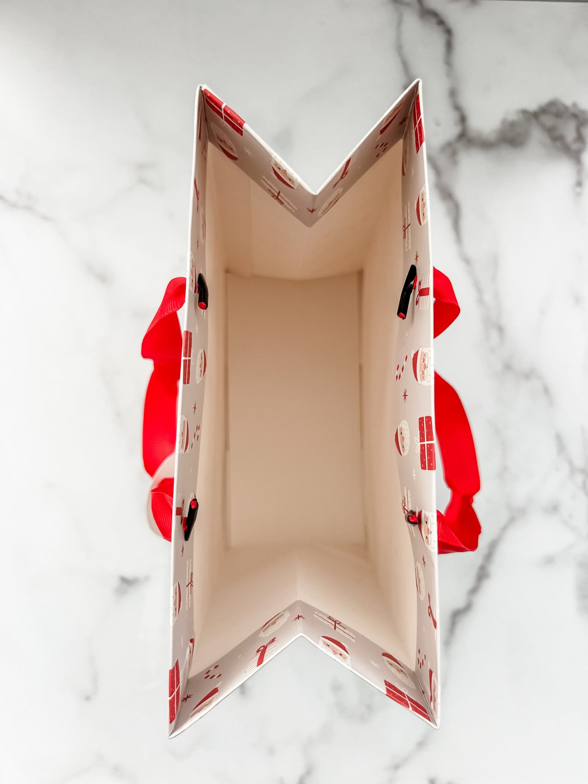 A festive Santa Claus design gift bag with a red ribbon handle.