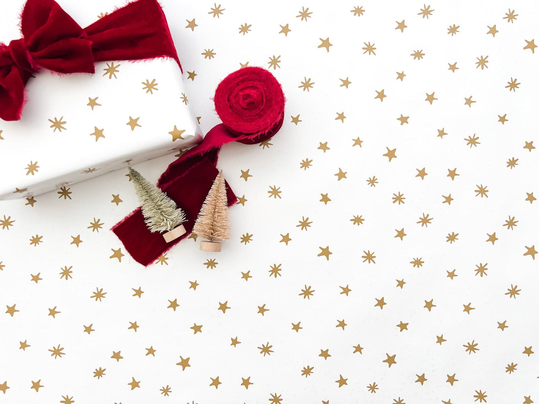 A roll of gold star wrapping paper with a bow, arranged on a white background.