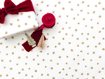 A roll of gold star wrapping paper with a bow, arranged on a white background.