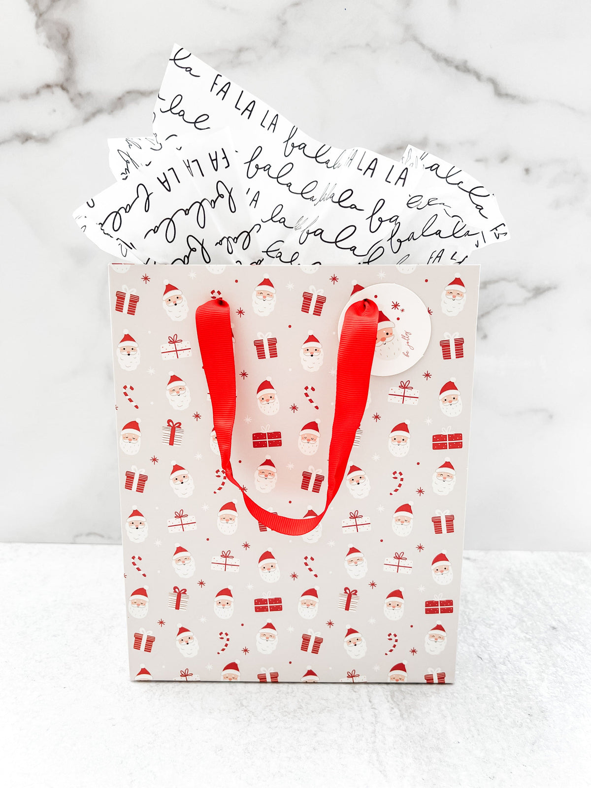 A festive Santa Claus design gift bag with a red ribbon handle and a round tag on the top right corner, featuring a pattern of Santa Claus.