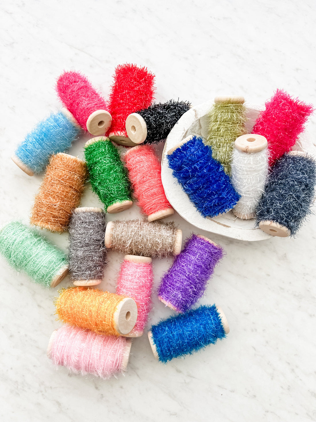 A collection of spools of tinsel in various colors scattered around, with wooden spool caps visible.