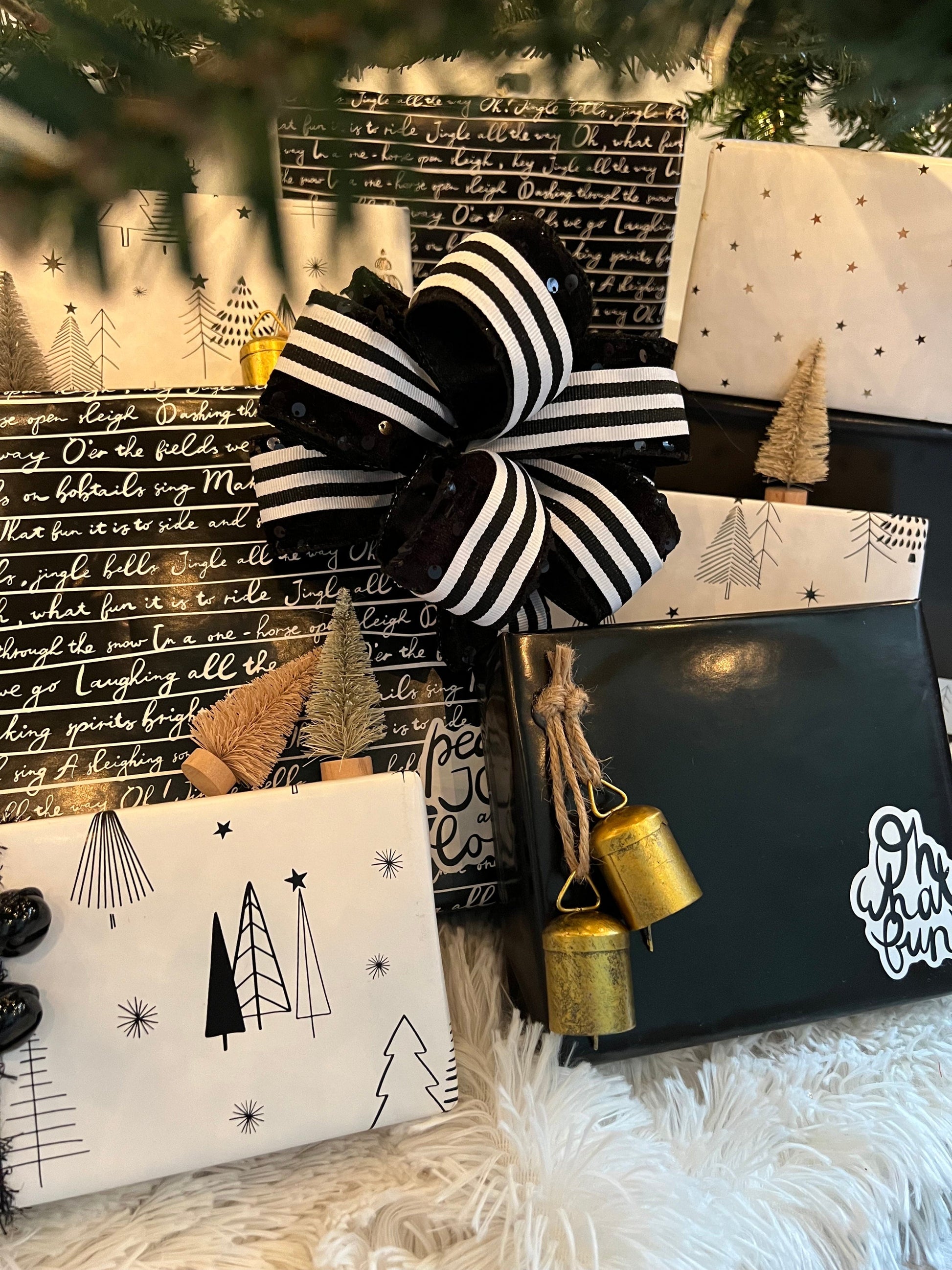 Gifts wrapped in black and white paper with a large striped ribbon and small bottle brush trees.