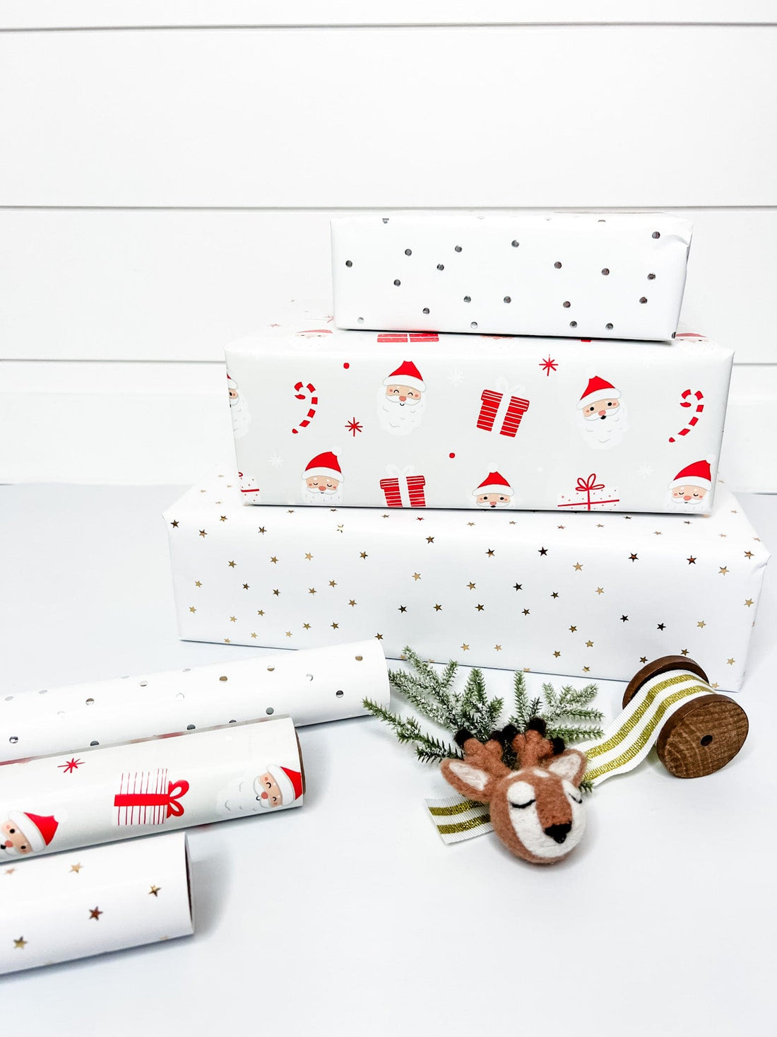 Three rolls of wrapping paper with Santa Claus design, metallic gold stars, and metallic silver dots, placed on a marble surface.